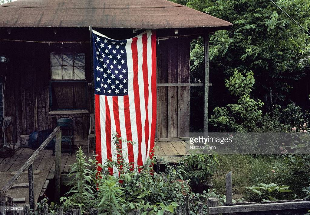 american-flag-is-displayed-on-the-front-porch-of-a-rundown-wooden-in-picture-id534289638.jpg